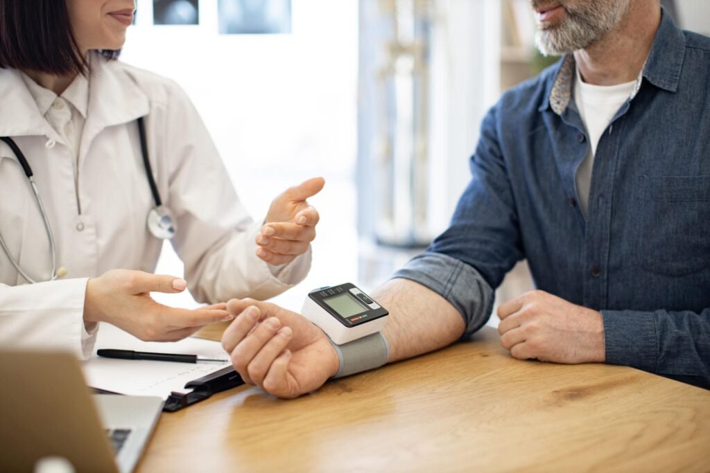 Doctor explaining home blood pressure monitoring to an older adult using a digital wrist blood pressure monitor for accurate BP readings, hypertension management, and cardiovascular health tracking.