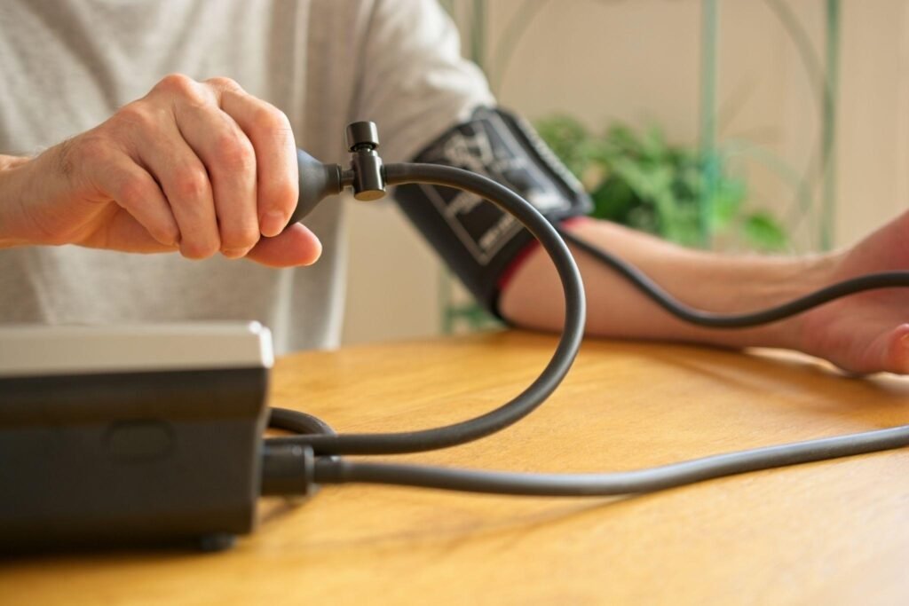 Close-up view of a person operating a semi-automatic digital blood pressure monitor by pumping the hand bulb with a cuff around their upper arm.